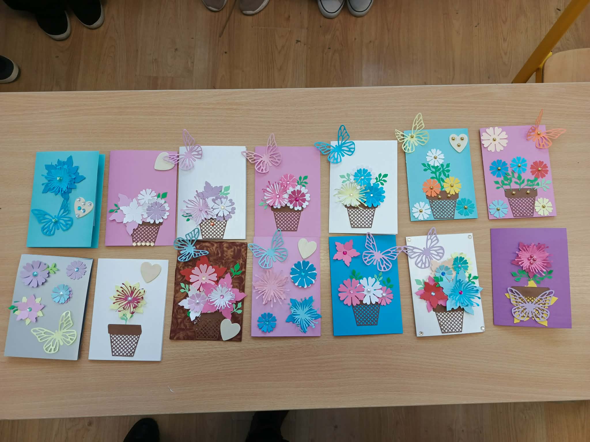 Na stole ułożone są gotowe kartki dla Babci i Dziadka, ozdobione kwiatami i motylami z kolorowego papieru.